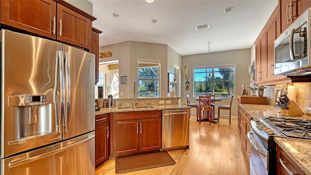 kitchen featuring sink, hanging light fixtures, stainless steel appliances, light stone counters, and light hardwood / wood-style floors