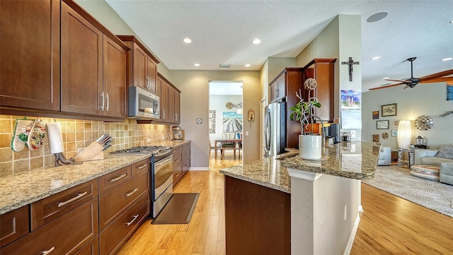 kitchen featuring stainless steel appliances, light stone counters, light hardwood / wood-style flooring, backsplash, and a textured ceiling