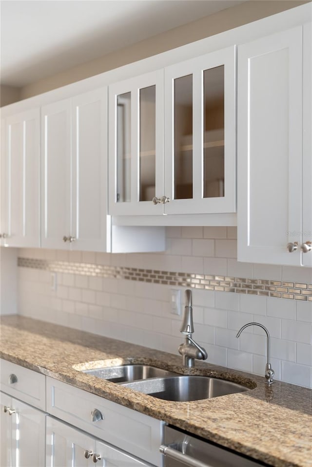 kitchen with white cabinets, decorative backsplash, light stone counters, and sink