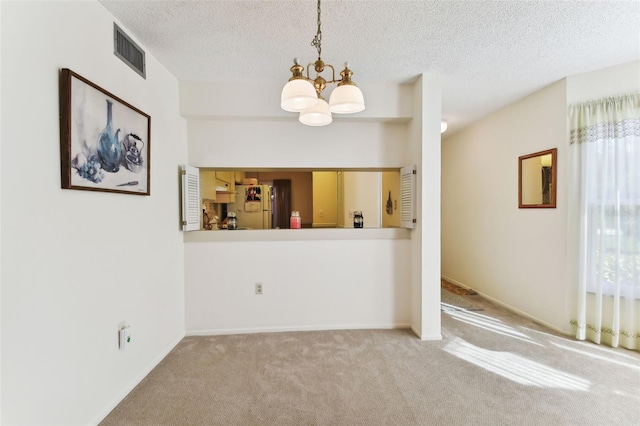 carpeted spare room featuring a textured ceiling and a notable chandelier