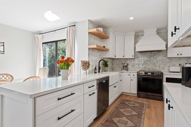 kitchen with premium range hood, white cabinets, sink, light hardwood / wood-style flooring, and stainless steel appliances