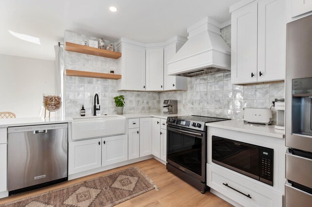 kitchen with sink, premium range hood, appliances with stainless steel finishes, white cabinets, and light wood-type flooring