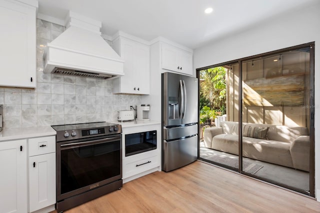 kitchen with custom exhaust hood, backsplash, light wood-type flooring, white cabinetry, and stainless steel appliances