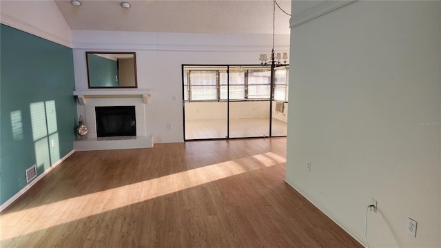 unfurnished living room featuring a textured ceiling, a tile fireplace, an inviting chandelier, hardwood / wood-style floors, and lofted ceiling