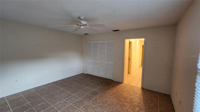 unfurnished bedroom with a textured ceiling, dark tile patterned flooring, a closet, and ceiling fan