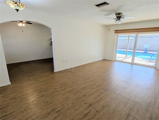 empty room featuring a ceiling fan, arched walkways, visible vents, and dark wood finished floors