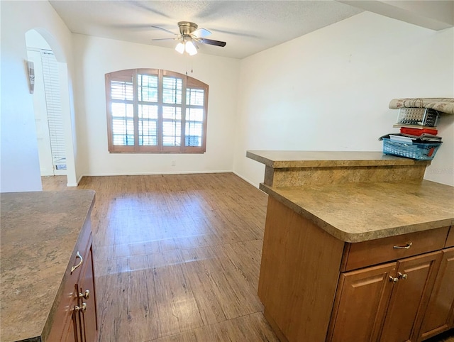 kitchen featuring brown cabinetry, arched walkways, light wood-style floors, and a ceiling fan