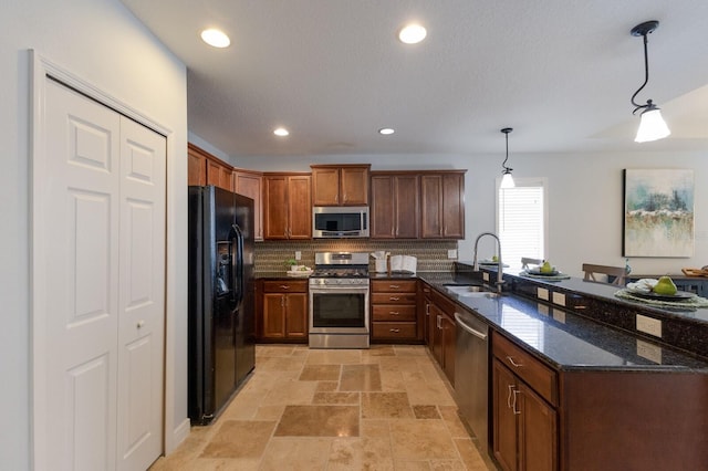 kitchen featuring sink, hanging light fixtures, dark stone countertops, decorative backsplash, and appliances with stainless steel finishes