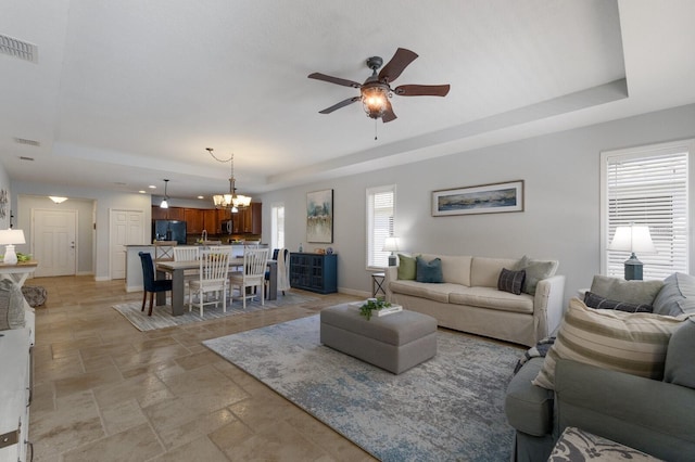 living room with ceiling fan with notable chandelier and a raised ceiling