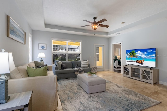 living room featuring a tray ceiling, ceiling fan, and a textured ceiling