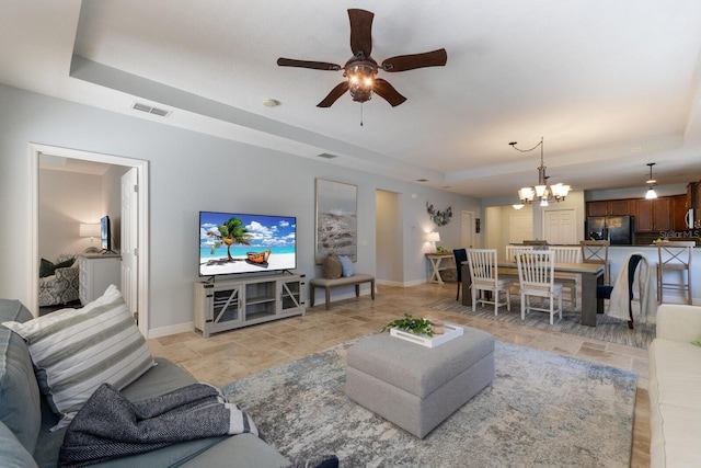 living room with a tray ceiling and ceiling fan with notable chandelier