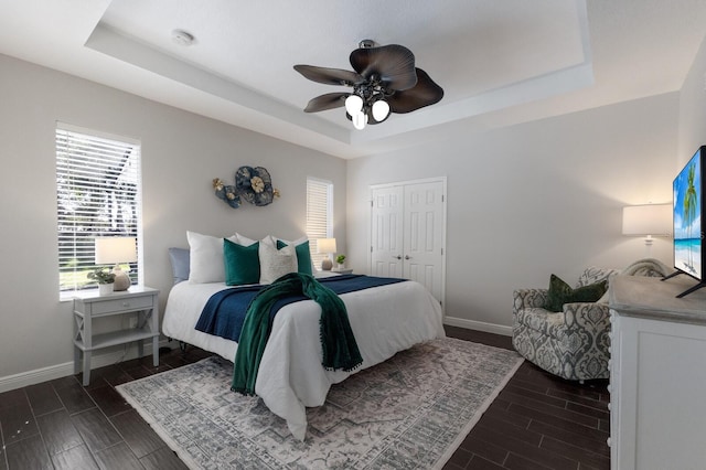 bedroom featuring a tray ceiling, ceiling fan, a closet, and dark wood-type flooring