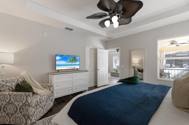 bedroom with ceiling fan, ensuite bathroom, and a tray ceiling