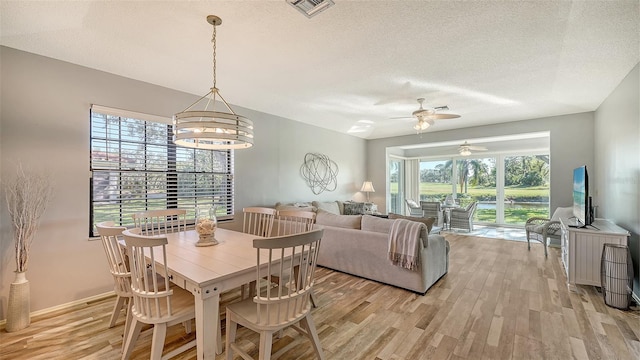 dining area with a textured ceiling, a wealth of natural light, light hardwood / wood-style flooring, and ceiling fan with notable chandelier