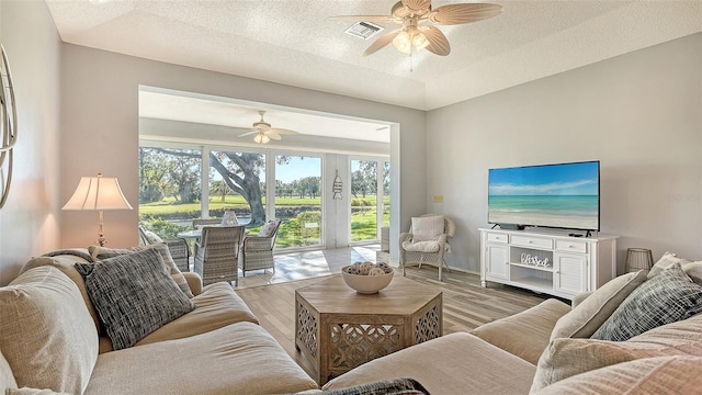 living room with ceiling fan, light hardwood / wood-style floors, and a textured ceiling