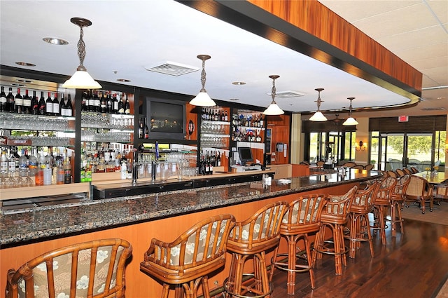 bar featuring dark hardwood / wood-style flooring, hanging light fixtures, and dark stone counters