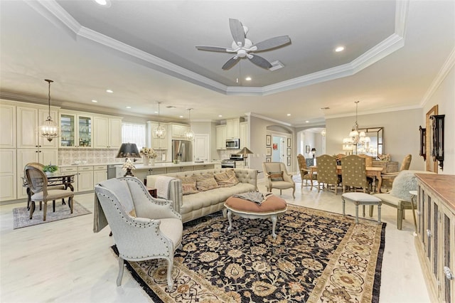 living room featuring a tray ceiling, crown molding, and ceiling fan with notable chandelier