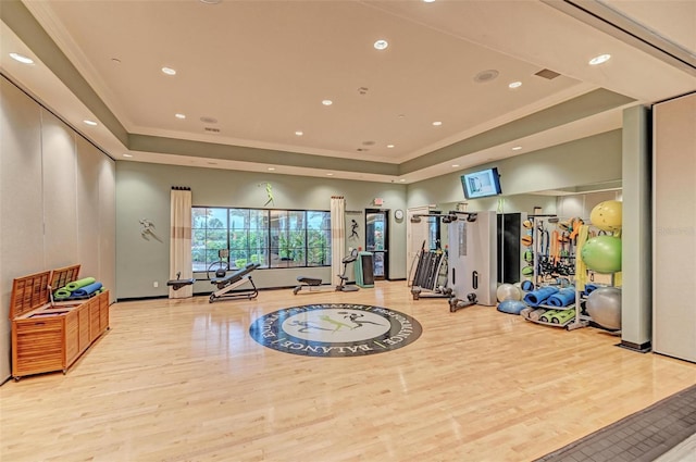 gym featuring light wood-type flooring, a tray ceiling, and ornamental molding