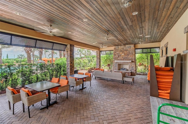 sunroom / solarium featuring a wealth of natural light, ceiling fan, wooden ceiling, and an outdoor stone fireplace