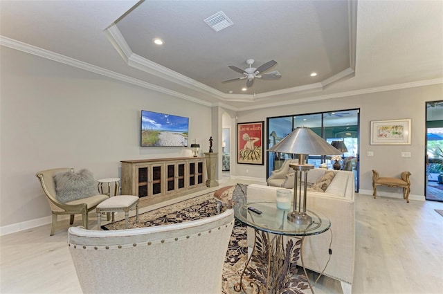 living room featuring ceiling fan, ornamental molding, a tray ceiling, and light hardwood / wood-style flooring