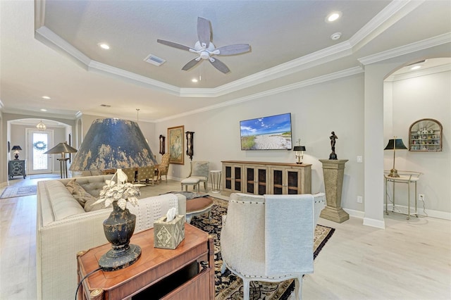 living room featuring a tray ceiling, light wood-type flooring, and ornamental molding