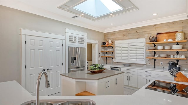 kitchen with a skylight, white cabinetry, a center island, stainless steel appliances, and wooden walls