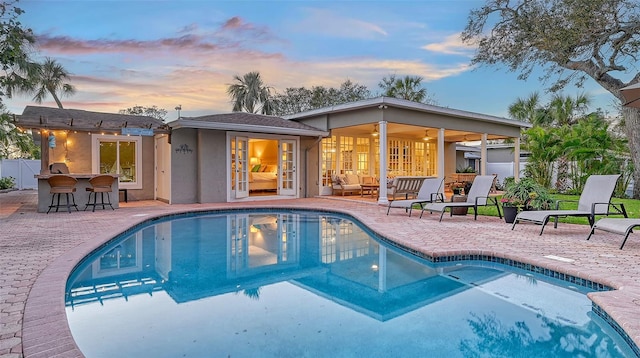 pool at dusk with a patio area and an outdoor bar