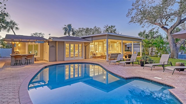 pool at dusk with outdoor lounge area, exterior bar, and a patio