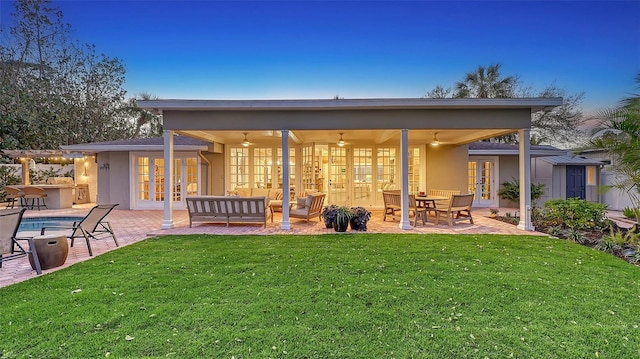 back house at dusk featuring a lawn, a patio area, an outdoor hangout area, and french doors