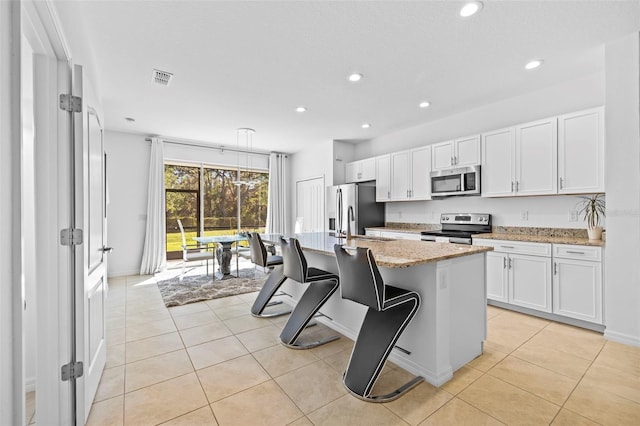 kitchen featuring white cabinetry, light stone counters, a breakfast bar, a center island with sink, and appliances with stainless steel finishes