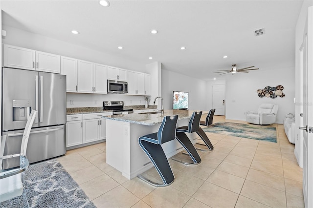 kitchen with white cabinetry, sink, light stone countertops, a center island with sink, and appliances with stainless steel finishes