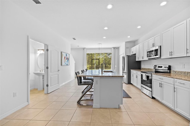 kitchen featuring white cabinetry, a kitchen breakfast bar, light stone counters, a kitchen island, and appliances with stainless steel finishes