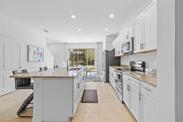 kitchen with a kitchen bar, a kitchen island with sink, white cabinets, and appliances with stainless steel finishes