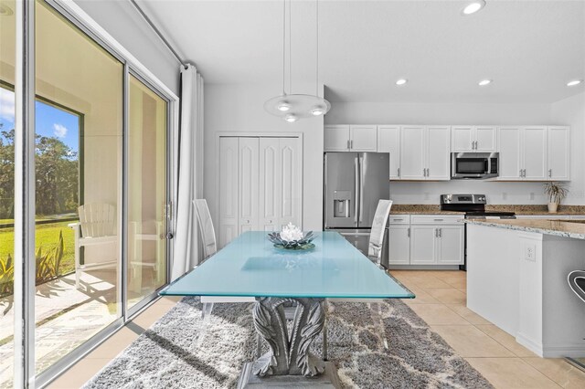 kitchen featuring pendant lighting, white cabinets, light tile patterned floors, appliances with stainless steel finishes, and light stone counters