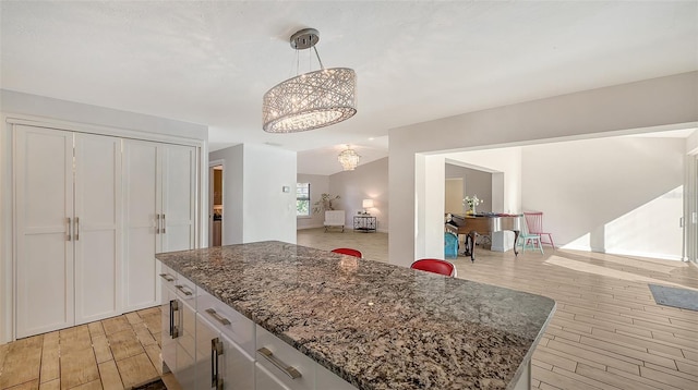 kitchen featuring pendant lighting, light hardwood / wood-style flooring, white cabinetry, dark stone countertops, and a center island