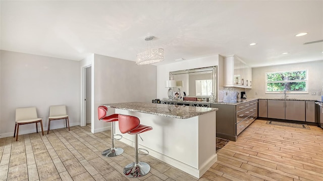 kitchen with pendant lighting, sink, a breakfast bar area, light stone counters, and decorative backsplash