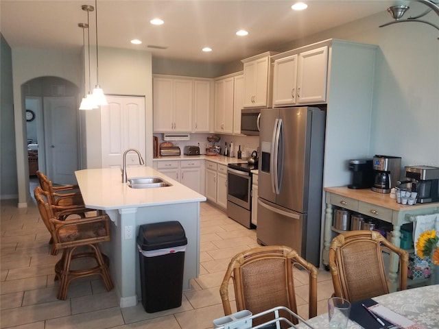 kitchen featuring a kitchen island with sink, white cabinets, sink, hanging light fixtures, and stainless steel appliances