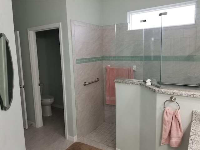 bathroom featuring tiled shower, vanity, tile patterned flooring, and toilet