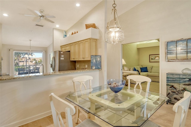 dining room featuring ceiling fan with notable chandelier, light hardwood / wood-style floors, and high vaulted ceiling