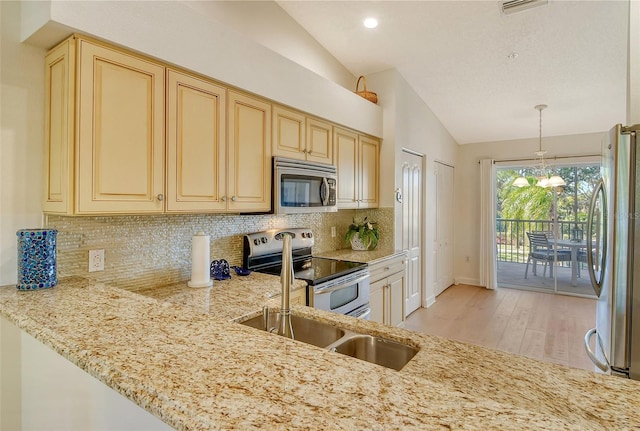 kitchen featuring backsplash, vaulted ceiling, light wood-type flooring, appliances with stainless steel finishes, and light stone counters