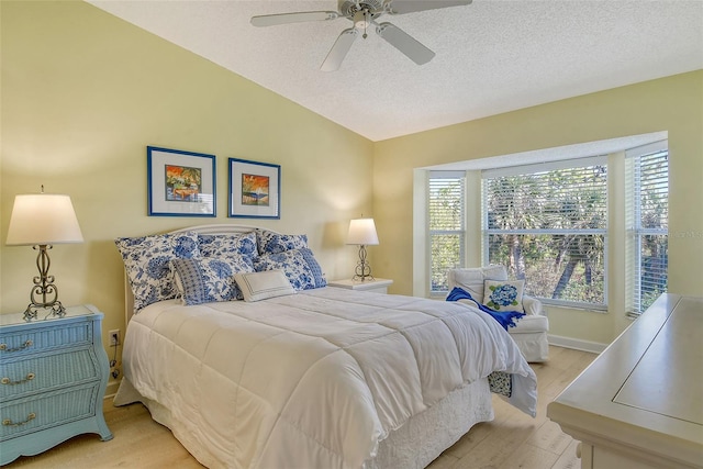 bedroom with a textured ceiling, ceiling fan, light hardwood / wood-style floors, and vaulted ceiling