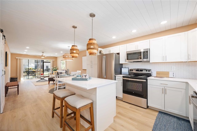 kitchen with tasteful backsplash, light hardwood / wood-style floors, white cabinetry, hanging light fixtures, and stainless steel appliances