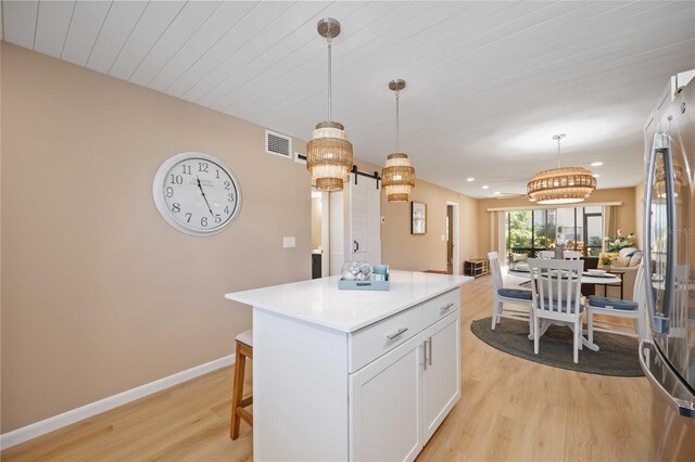 kitchen featuring decorative light fixtures, white cabinets, a barn door, a kitchen island, and stainless steel refrigerator