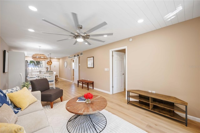 living room with ceiling fan, a barn door, and light hardwood / wood-style flooring