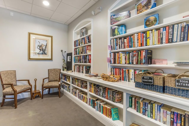 living area with a paneled ceiling, built in shelves, and carpet floors