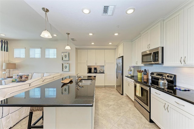 kitchen with appliances with stainless steel finishes, sink, white cabinets, hanging light fixtures, and an island with sink