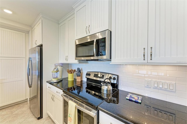 kitchen with light tile patterned floors, stainless steel appliances, white cabinetry, and dark stone countertops