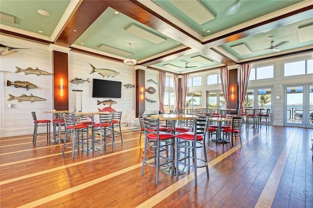 dining room featuring wood walls, coffered ceiling, ceiling fan, beamed ceiling, and wood-type flooring