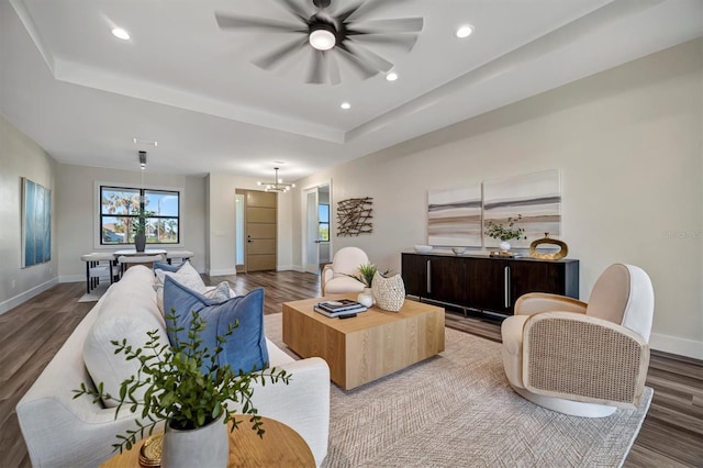 living room with a raised ceiling, hardwood / wood-style floors, and ceiling fan with notable chandelier