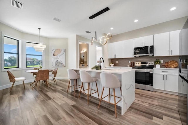 kitchen with light wood-type flooring, white cabinetry, stainless steel appliances, and a kitchen island with sink